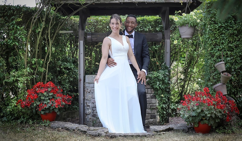 Couple de mariés souriant et heureux dans un jardin fleuri, près d'un puits, la mariée en robe blanche, le marié en costume.