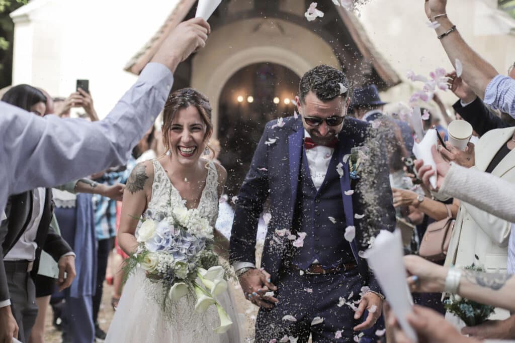 Mariés joyeux sortant de l'église sous une pluie de pétales et confettis lancés par les invités.