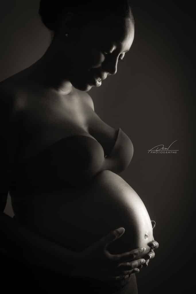 Femme enceinte de profil en noir et blanc, mains posées tendrement sur son ventre. Signature Aurion PHOTOGRAPHE.